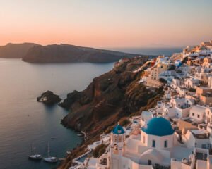 Santorini budget travel tips aerial view of caldera with white buildings and blue domes at sunset